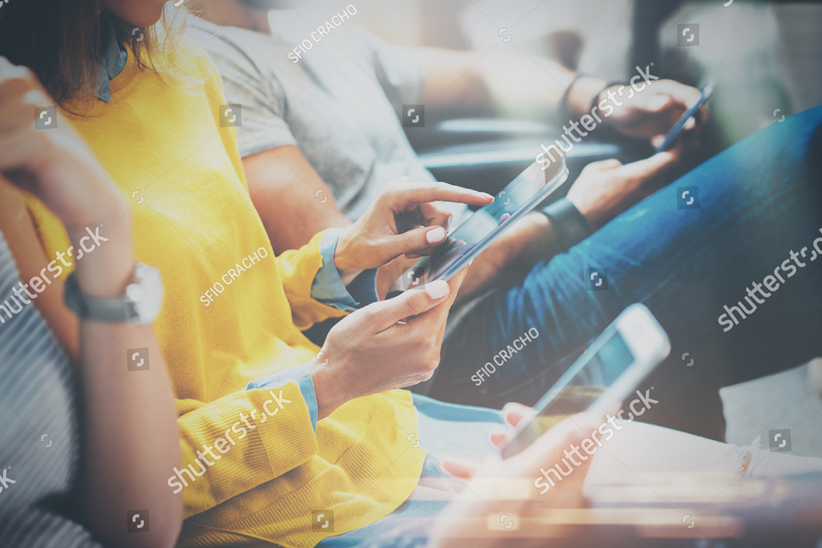 stock-photo-group-of-young-hipsters-sitting-on-sofa-holding-en-hands-and-using-digital-tablet-smartphone-573110821